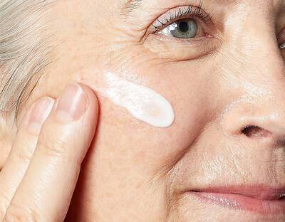 Altere Frau cremt ihre Wange ein