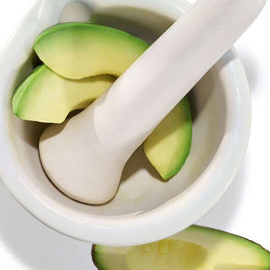 Morser mit Stoßel und Avocadoscheiben, die zur Zubereitung bereit sind, vor weißem Hintergrund.