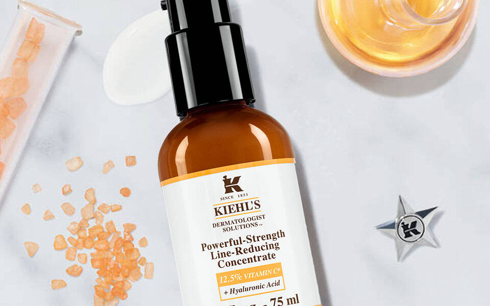 Alt-Text: Eine Anordnung von Hautpflegeprodukten auf einem marmorierten Hintergrund, darunter ein braunes Serum, eine orangefarbene Olflasche und ein lila Pumpspender, umgeben von dekorativen Elementen.