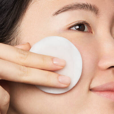Eine Frau reinigt ihr Gesicht mit einem Wattepad, das sanft auf ihrer Haut gleitet.