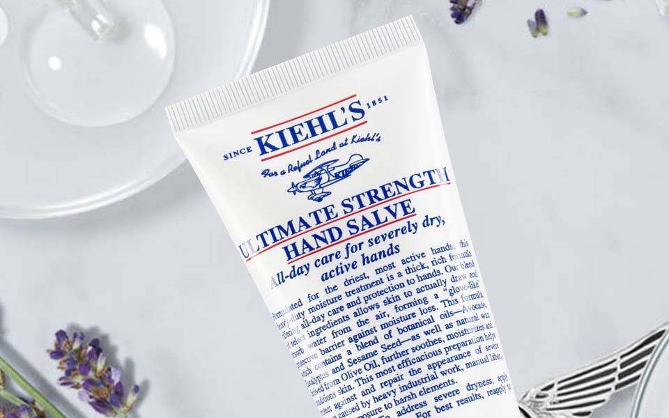 Eine Hand halt einen kleinen Klecks Creme uber einem weißen Hintergrund, auf dem ein Kiehl's Produkt sichtbar ist.