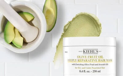 Kiehls Haarmaske mit Oliven- und Avocadool, umgeben von einer halben Avocado und einer Morser.