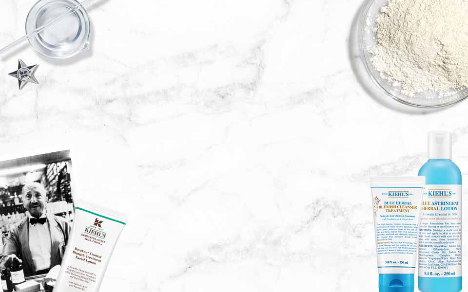Kiehl's Produkte (Reiniger, Adstringens) und historische Elemente (Mann, Messbecher) auf weißem Marmorhintergrund.