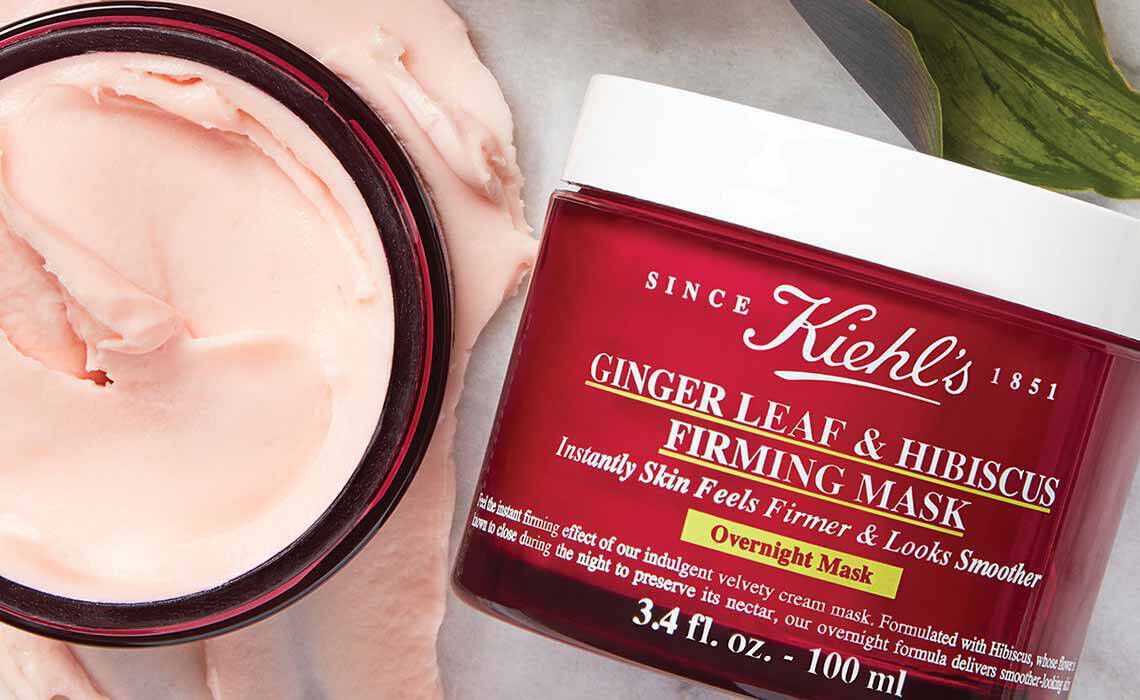 Ein offener Tiegel mit Kiehl's Ginger Leaf & Hibiscus Firming Mask (rote Verpackung) mit sichtbarer rosafarbener Creme daneben.