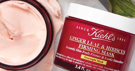 Ein offener Tiegel mit Kiehl's Ginger Leaf & Hibiscus Firming Mask (rote Verpackung) mit sichtbarer rosafarbener Creme daneben.