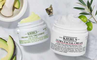 Zwei Kiehls-Cremetopfe: Avocado-Augenbehandlung und Ultra Feuchtigkeitscreme, umgeben von Avocado und Oliven.