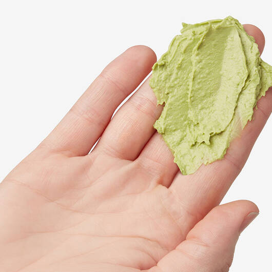 Eine Handflache halt einen Klecks gruner Creme, wahrscheinlich eine Avocado-Maske oder ein Kosmetikprodukt, auf weißem Hintergrund.