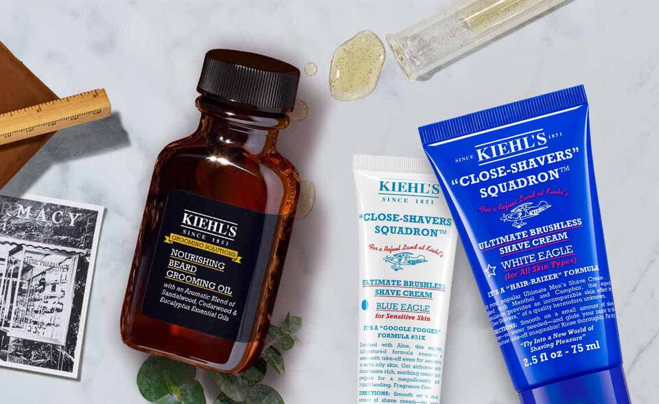 Produktauswahl von Kiehl's, bestehend aus einer Gesichtscreme, Rasiercreme und einem Gesichtsserum auf einem marmorierten Hintergrund.