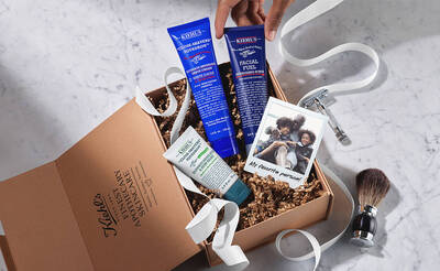 Geschenkbox mit Kiehl's Hautpflegeprodukten, einer Rasiermaschine und einem Foto von lachelnden Menschen auf Marmorhintergrund.