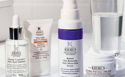 Enthalt vier Kiehl's Hautpflegeprodukte: Serum, Sonnencreme, Retinol-Serum und Gesichtscreme, auf einem Tisch mit Wasser.