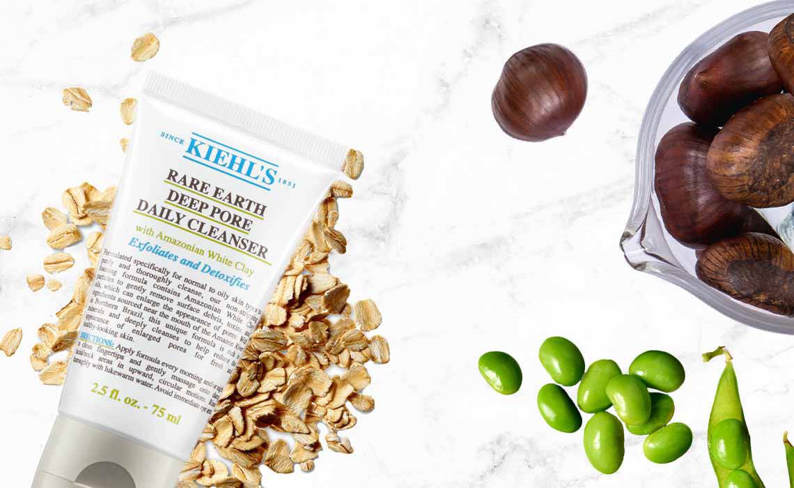 Eine Tube Hafer-Feuchtigkeitspflege auf marblisiertem Hintergrund, umgeben von Haferflocken, grunen Trauben und Kastanien.