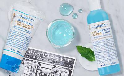 Kiehl's Hautpflegeprodukte: blauer Krauterreiniger und astringierende Lotion, umgeben von Wasser und einer alten Apotheke.