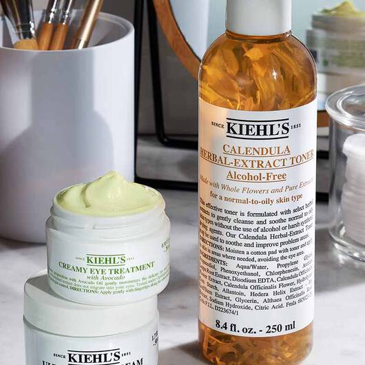 Kiehl's Produkte auf einem Waschtisch: Calendula Toner, Creamy Eye Treatment und ein weiteres Produkt, umgeben von Kosmetikzubehor.