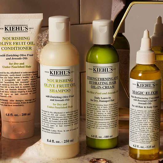 Eine Reihe von Kiehl's Haarpflegeprodukten (Shampoo, Spulung, Ole) mit Oliven- und Avocadool auf einem Waschtisch arrangiert.