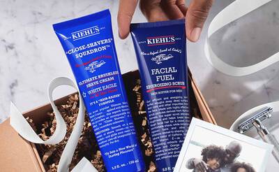 Zwei Kiehl's Pflegeprodukte fur Manner in einer Geschenkbox: Rasiercreme und Energieschrub, umgeben von Holzwolle.