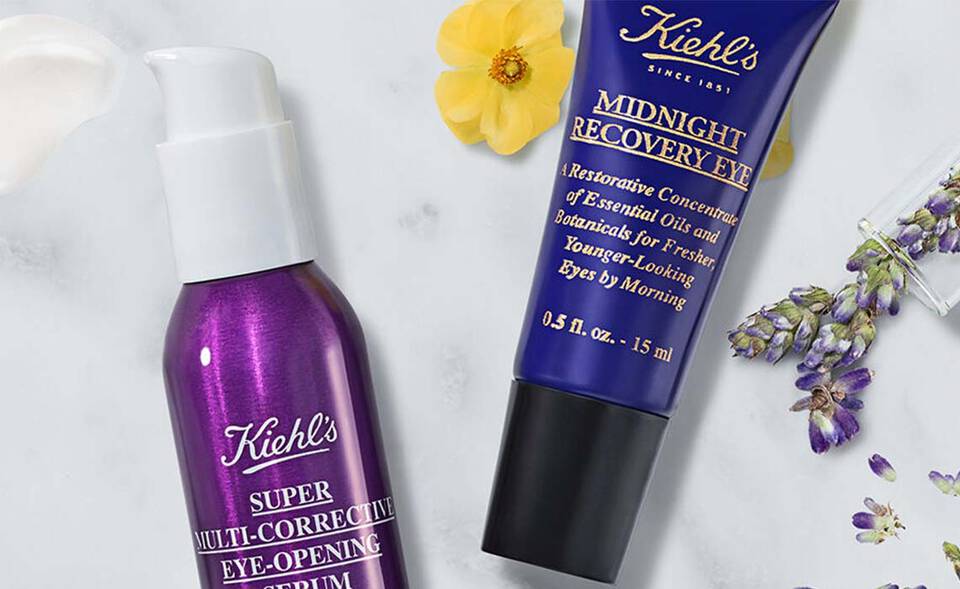 Hintergrund aus Marmor mit Kiehl's Hautpflegeprodukten: einer Creme, einem Serum und einem Spray, umgeben von Avocado und Lavendel.