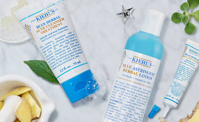 Produkte von Kiehl's: Blue Herbal Acne Cleanser Treatment und Blue Astringent Herbal Lotion auf einem marmorierten Hintergrund.