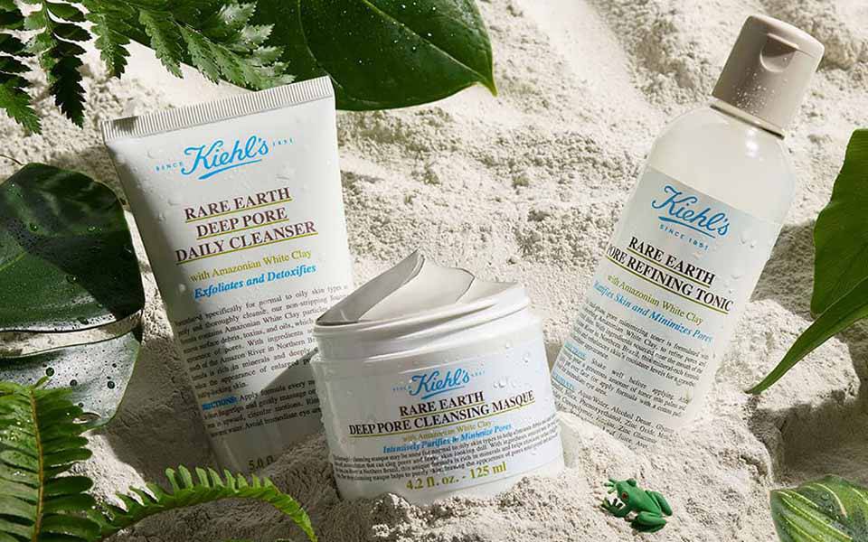 Alt-Text: Ein marblesierter Hintergrund mit einer Tube Kiehl's Produkt und einem offenen Krug mit grauer Creme.