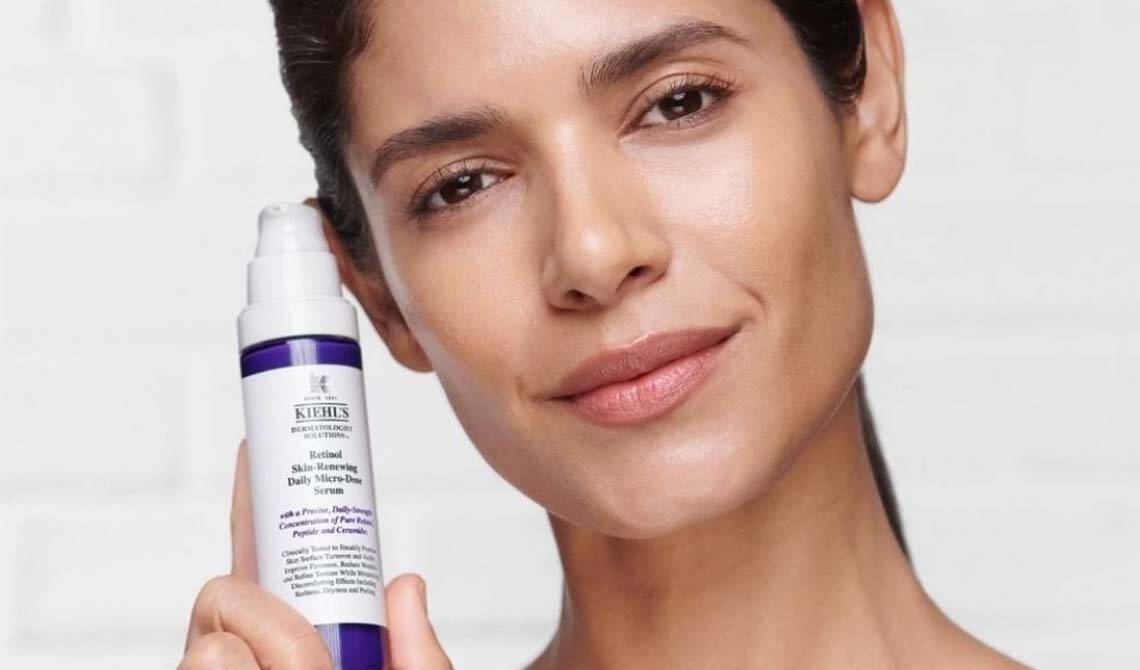 Gesicht einer Frau, die das Kiehl‘s Retinol Tagesserum in der Hand halt