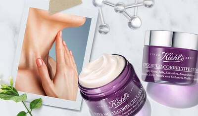 A close-up of a hand gently touching skin, alongside Kiehl's Super Multi-Corrective Cream jar and a polaroid-style photo. The scene features a light background with green foliage accents.