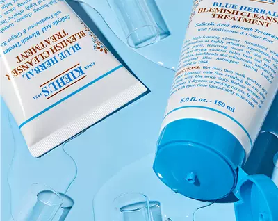 Creme et gel de traitement contre les imperfections Kiehl's sur fond bleu, accompagnes de gouttes d'eau.