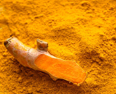 A piece of fresh turmeric root sits on a bed of bright yellow turmeric powder.