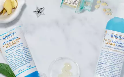 Eine Anordnung von Kiehl's Hautpflegeprodukten auf einer marmorierten Flache, umgeben von frischen Zutaten wie Minze und Ingwer.