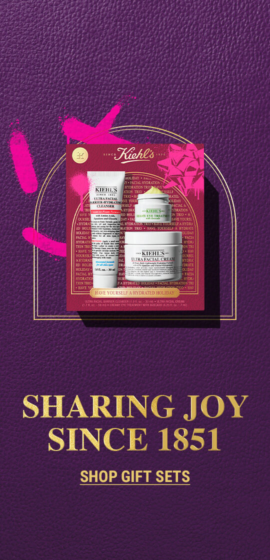 Auf der linken Seite befinden sich zwei Kiehl’s-Geschenksets fur die Feiertage. Links ist eine weinrote und pinke Geschenkbox mit einer Tube „KIEHL’S ULTRA FACIAL CLEANSER“, einem Tiegel „KIEHL’S CREAMY EYE TREATMENT WITH AVOCADO“ und einem Tiegel „KIEHL’S ULTRA FACIAL CREAM“. Rechts ist eine blau-grune Geschenkbox mit einem Tiegel „KIEHL’S ULTRA FACIAL CREAM“ und einem Tiegel „KIEHL’S ULTRA BODY MEGA MOISTURIZER SQUALANE CREAM“. Beide Boxen sind festlich dekoriert. Die rechte Seite der Grafik zeigt einen einfarbig violetten Hintergrund mit weißem Text: „SET-SATIONELLE GESCHENKE ZUM VERSCHENKEN“ und darunter in kleinerer Schrift „JETZT ENTDECKEN“.