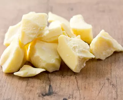 Chunks of pale yellow shea butter scattered on a wooden surface.