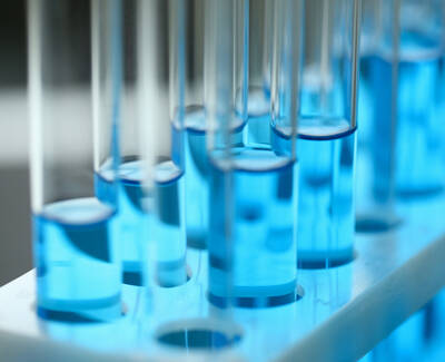 A close-up of test tubes filled with blue liquid, arranged in a test tube rack. The background is softly blurred.