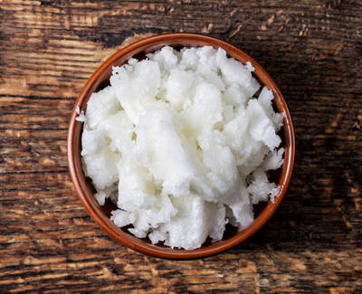A small brown bowl filled with white, fluffy coconut or shea butter on a wooden surface.
