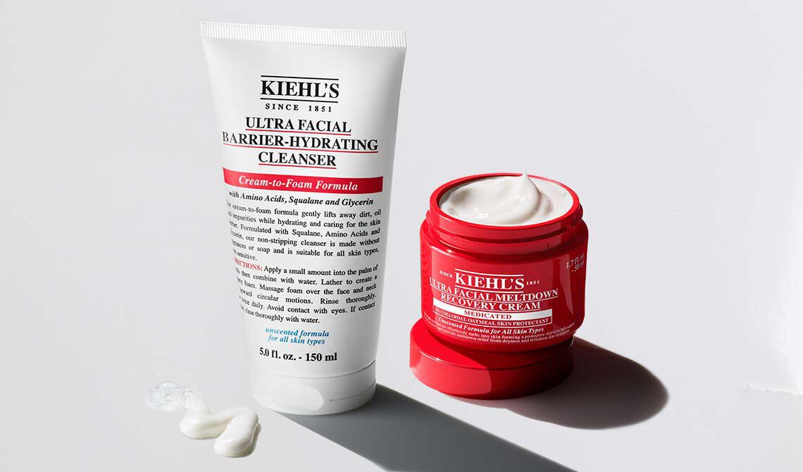 Two Kiehl's Ultra Facial skincare products: a white tube of Barrier-Hydrating Cleanser and an open red jar of Meltdown Recovery Cream on a white background.