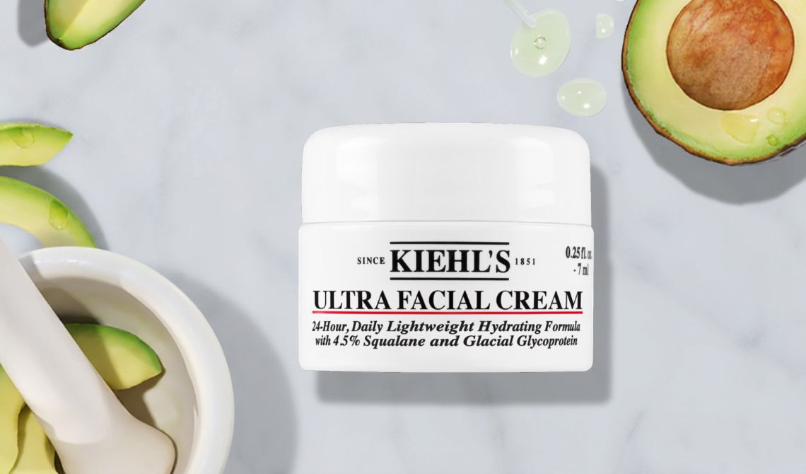 Produktbild der Kiehl's Ultra Facial Cream, leichte 24-Stunden-Feuchtigkeitsformel mit 4,5% Squalan und Gletscherprotein (7 ml), prasentiert auf grauem Marmorhintergrund mit frischen Avocadoscheiben und Serumtropfen.