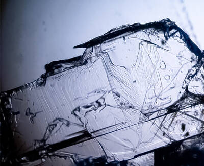 Close-up image of a transparent crystal structure showing intricate patterns and textures. The light reflects off its surfaces, creating a unique visual appearance.