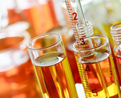 Close-up of laboratory glassware containing colorful liquids, including test tubes and a graduated cylinder, with vibrant hues of orange and yellow.