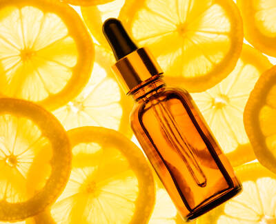 An amber glass dropper bottle lies on top of vibrant lemon slices, with a bright yellow background.