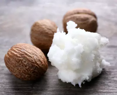 Four whole nutmeg seeds surrounding a dollop of white, fluffy nutmeg butter, resting on a textured wooden surface.