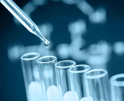 A close-up of a pipette dropping a liquid onto test tubes, set against a blurred background that resembles a DNA structure.