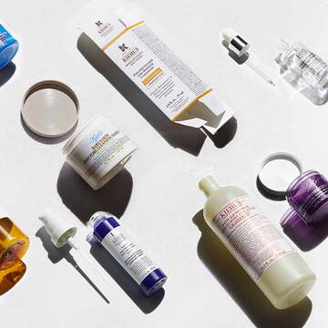 Une gamme de produits de soin presentee sur un fond clair, comprenant des flacons, des pots et des compte-gouttes de differentes couleurs et formes.