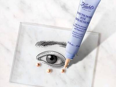 Un tube de traitement pour les yeux Kiehl's sur un fond marbre, avec trois perles de produit disposees en dessous.