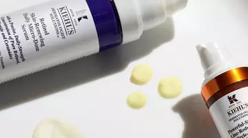 Alt-Text: Zwei Kiehl's Hautpflegeprodukte in Flaschen, daneben einige Tropfen des Inhalts auf einem weißen Untergrund.