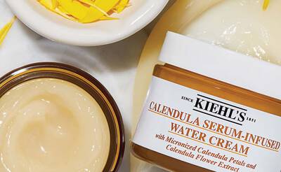 Creme hydratante a base de fleurs de calendula, avec des petales dans un pot en verre et un bol de petales de calendula a cote.