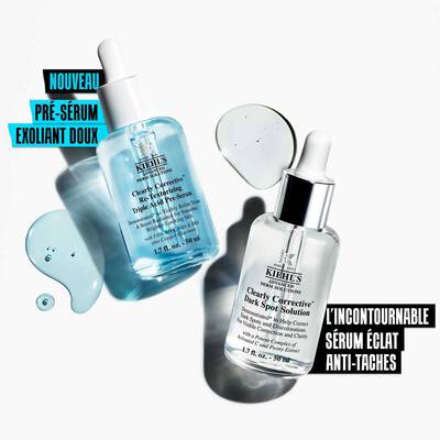 Alt-Text: Zwei Flaschchen von Kiehl's Hautpflegeprodukten auf einem hellen Hintergrund. Eines ist die "Clearly Corrective Dark Spot Solution" und das andere die "Clearly Corrective Daily Re-Texturizing Triple Acid Peel". Wassertropfchen sind rund um die Flaschchen verteilt.