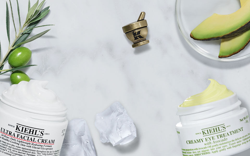 Creme hydratante et creme anti-age posees sur un marbre, entourees d'ingredients naturels tels que l'olive et la papaye.