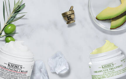 Creme hydratante et creme anti-age posees sur un marbre, entourees d'ingredients naturels tels que l'olive et la papaye.